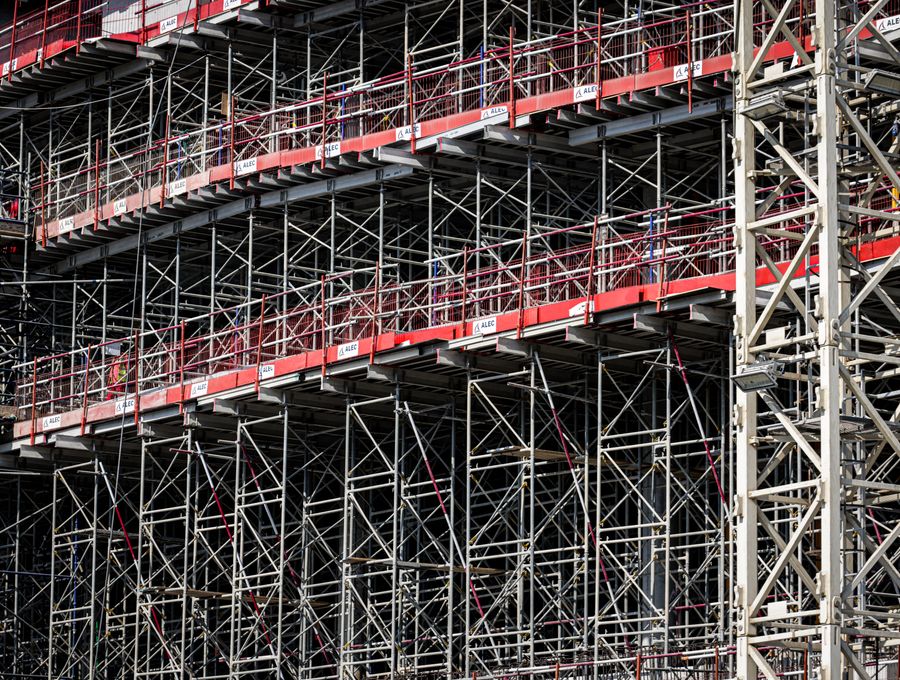 A tall system scaffold with red toe boards around a large building